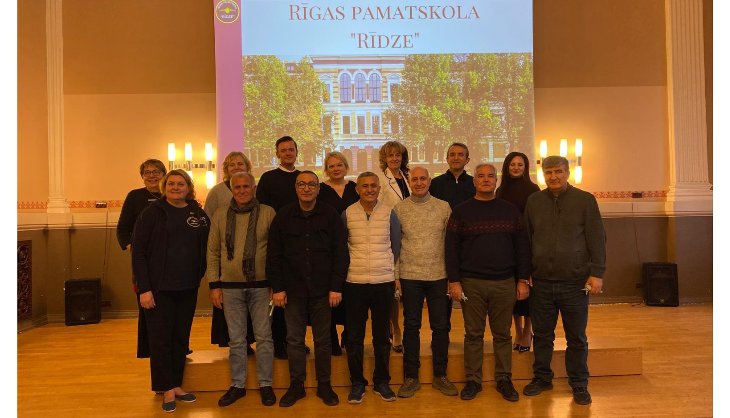 Turcijas delegācijas un pamatskolas "Rīdze" pārstāvji uz prezentācijas "Rīgas pamatskola "Rīdze"" fona